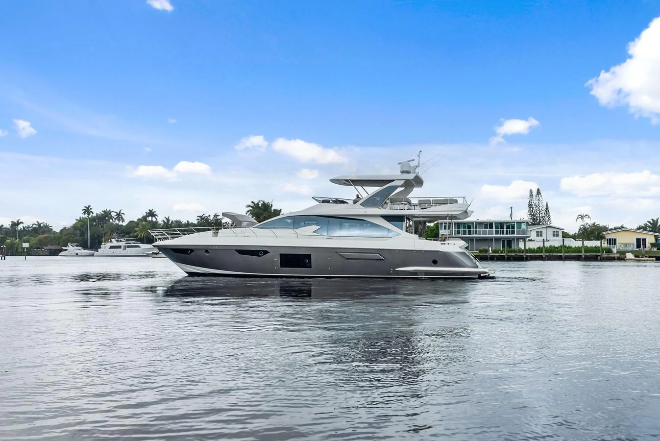 A sleek and modern yacht cruising on calm waters with a backdrop of waterfront homes. aboard CLASS DISMISSED Yacht for Sale
