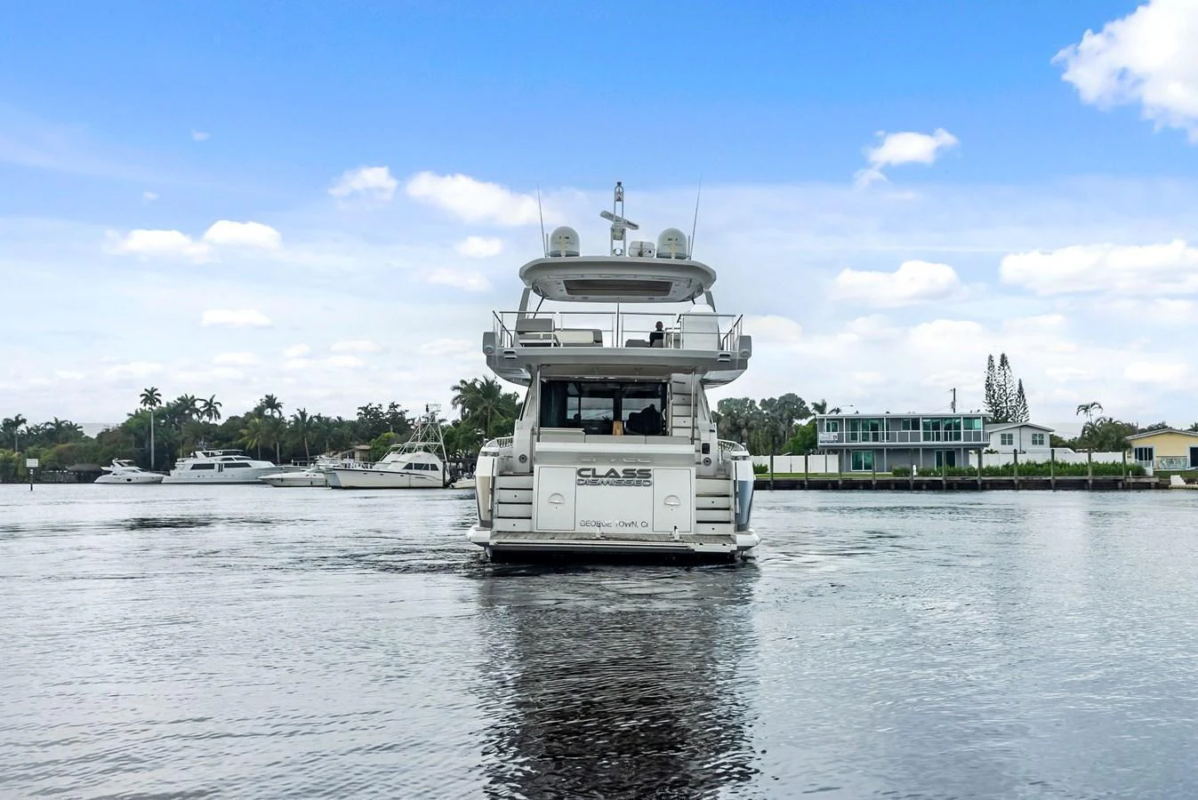 A luxurious yacht is seen from the rear, cruising on calm waters with a scenic waterfront backdrop. aboard CLASS DISMISSED Yacht for Sale