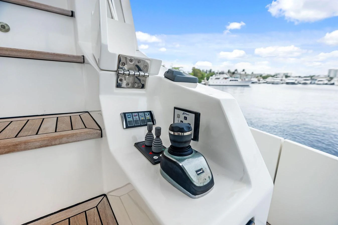 The image showcases a yacht's control station with a joystick and control panel, set against a serene marina backdrop. aboard CLASS DISMISSED Yacht for Sale