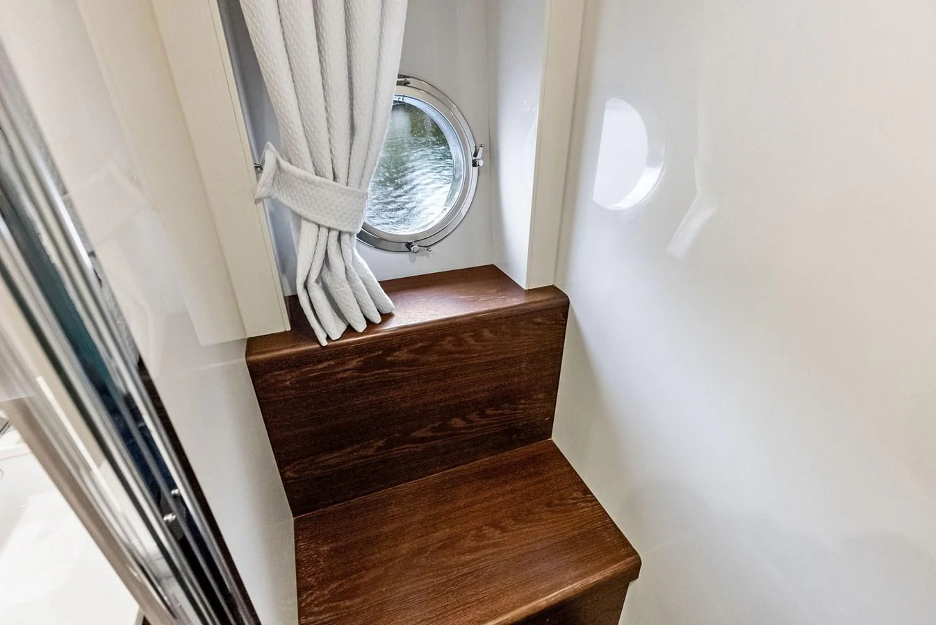 A cozy interior space featuring a small wooden bench and a porthole window with white curtains. aboard CLASS DISMISSED Yacht for Sale