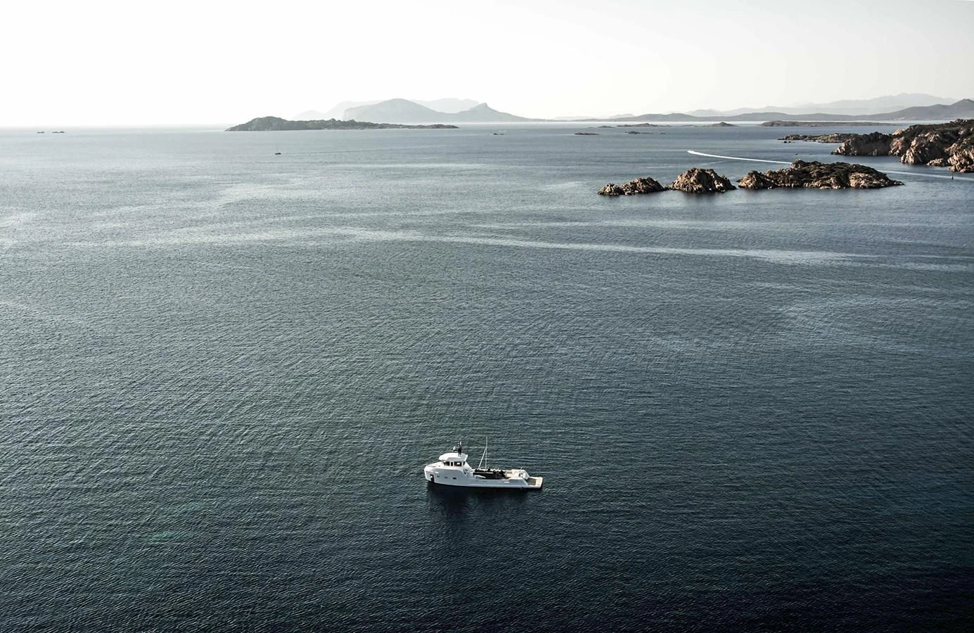 A serene yacht is anchored in a vast, calm sea with distant islands on the horizon. aboard 20 YXT Yacht for Sale