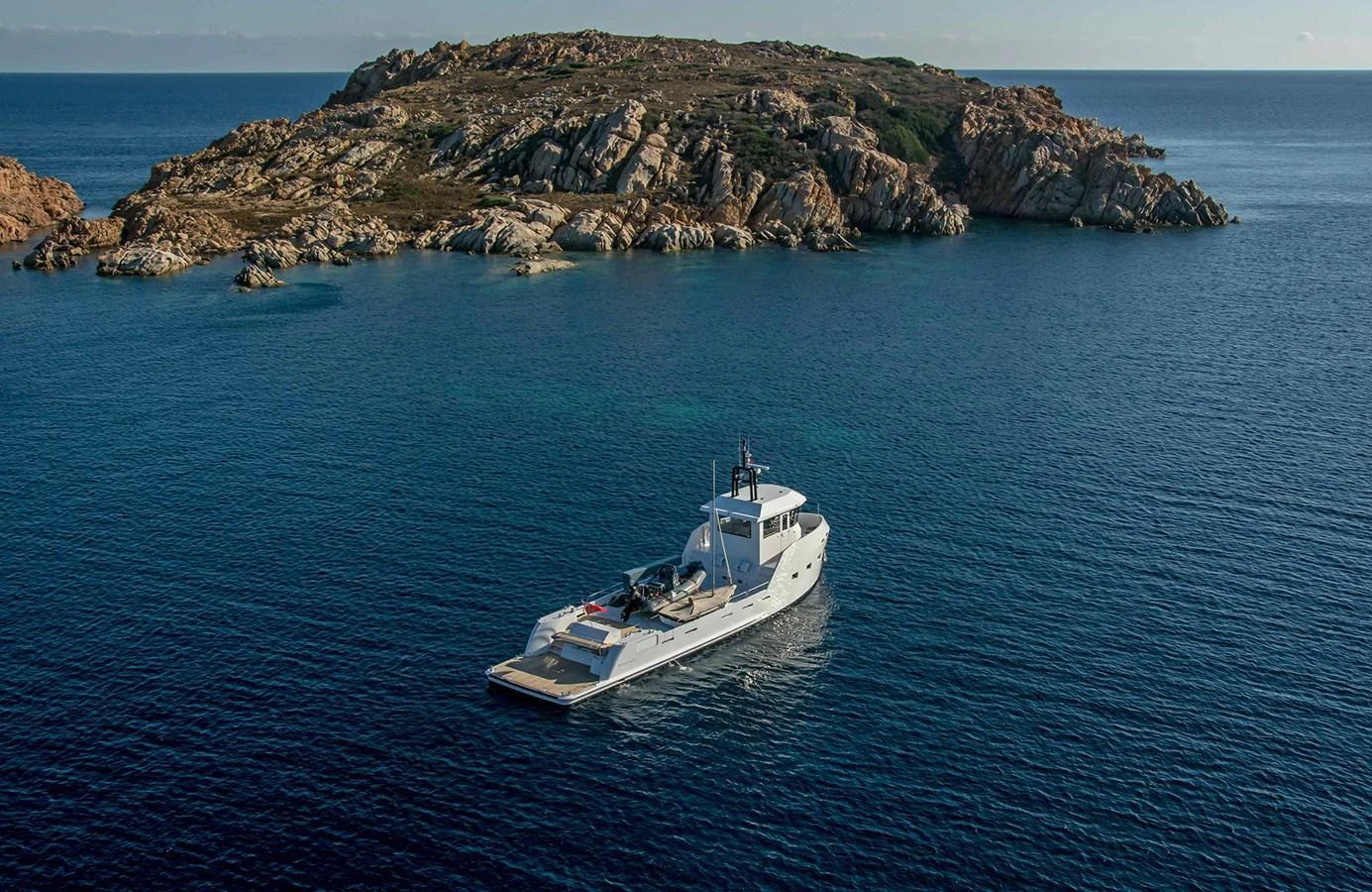 A sleek yacht cruises in tranquil blue waters near a rocky island. aboard 20 YXT Yacht for Sale