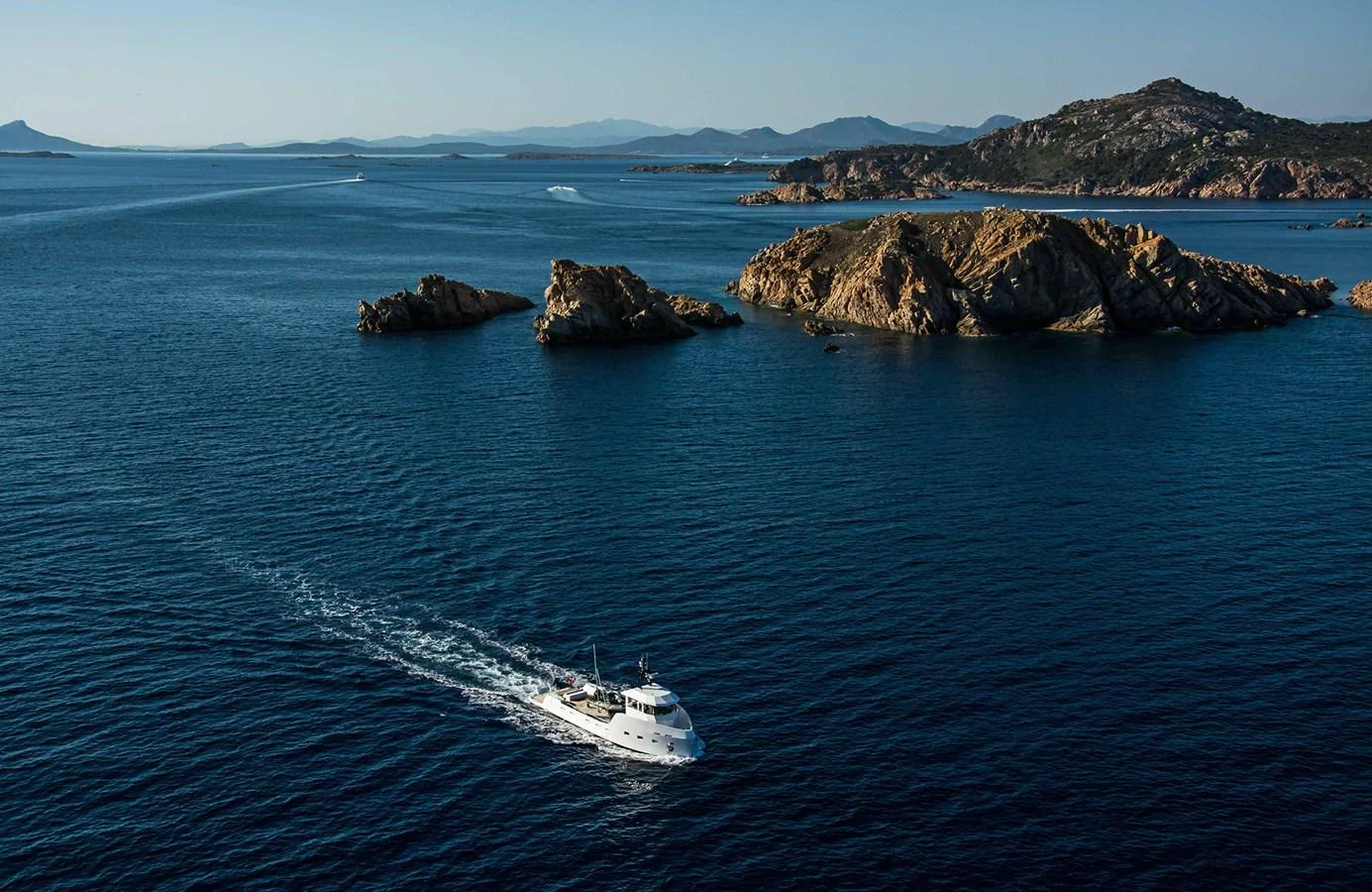 A sleek yacht cruises through serene blue waters with rocky islands in the background. aboard 20 YXT Yacht for Sale