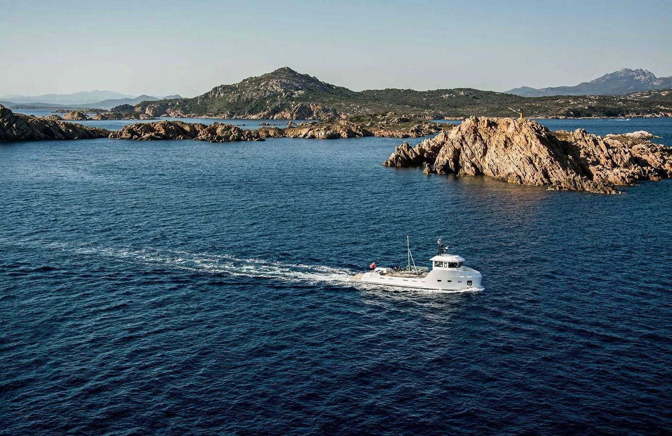 A sleek yacht cruises through serene blue waters with rocky islands in the background. aboard 20 YXT Yacht for Sale