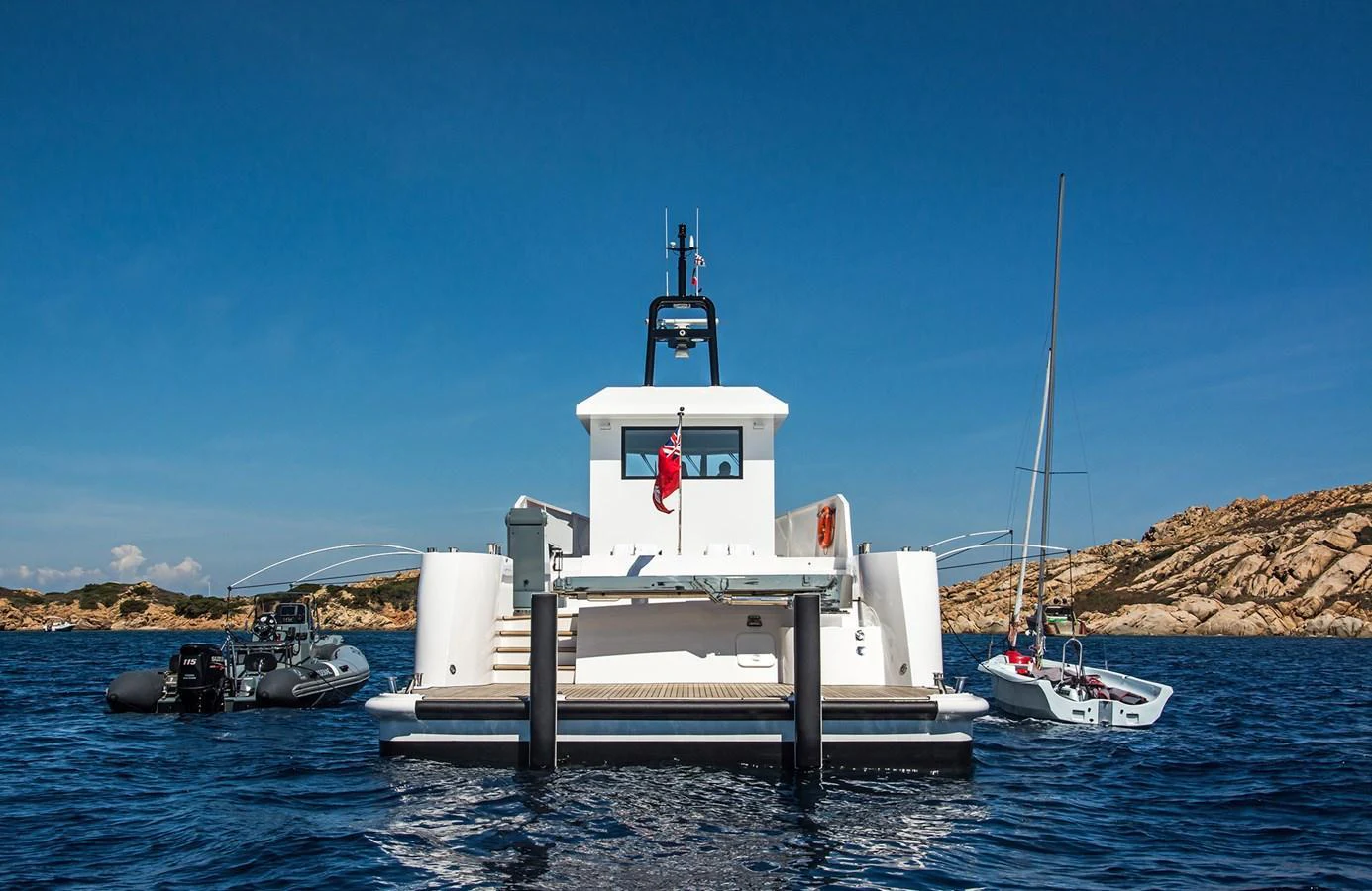 The yacht is anchored in a serene bay, accompanied by a tender and a small sailboat. aboard 20 YXT Yacht for Sale