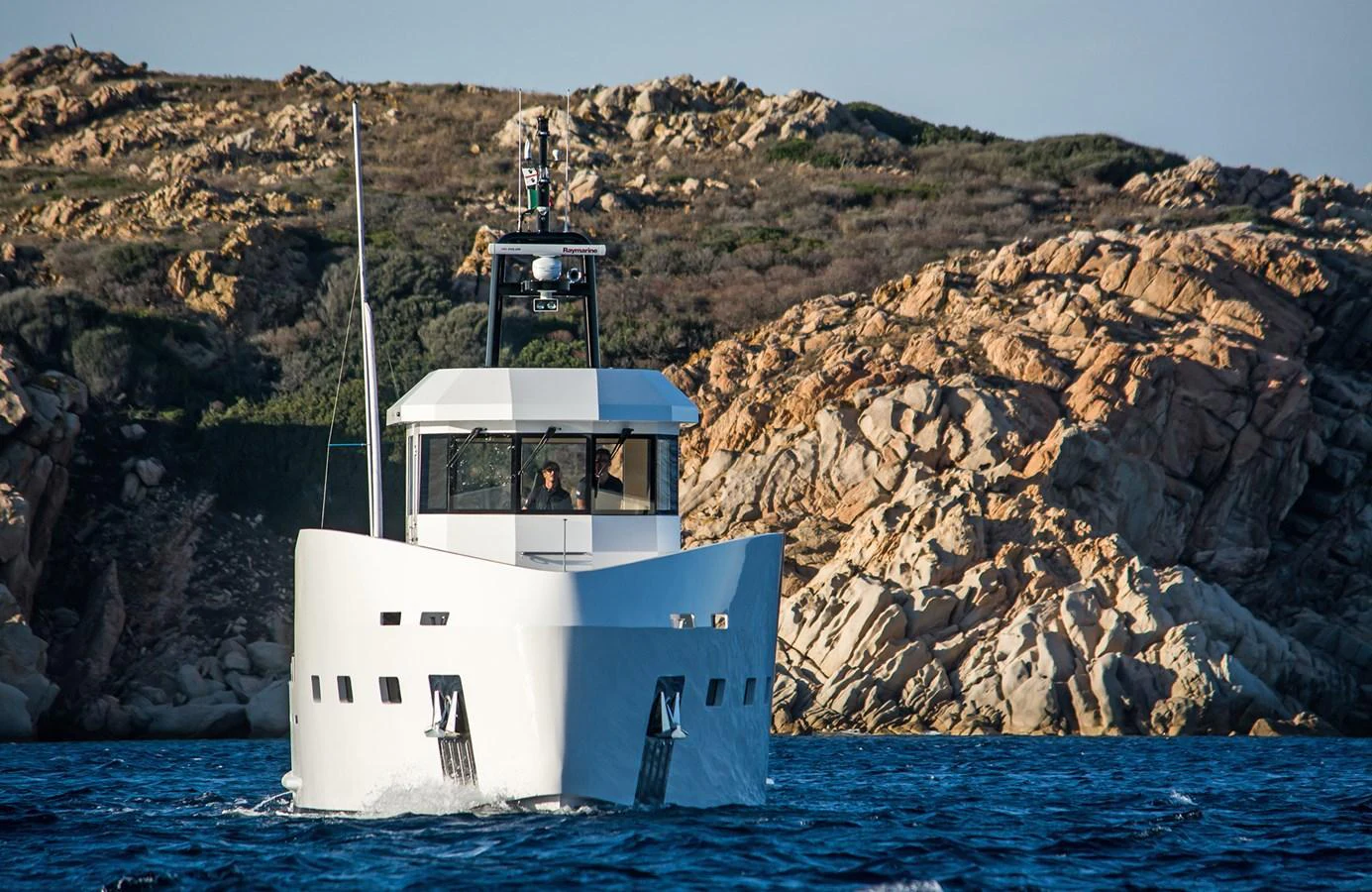 A modern yacht cruises through clear blue waters with a rocky coastline in the background. aboard 20 YXT Yacht for Sale