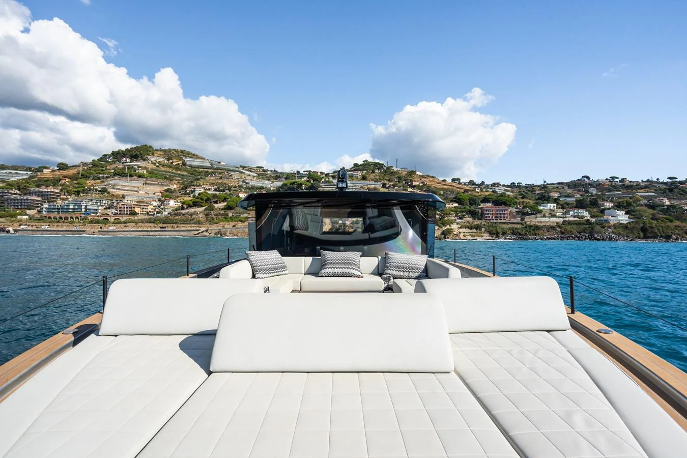 The yacht's foredeck features a spacious sunbathing area with plush cushions, set against a scenic coastal backdrop. aboard SIMON Yacht for Sale