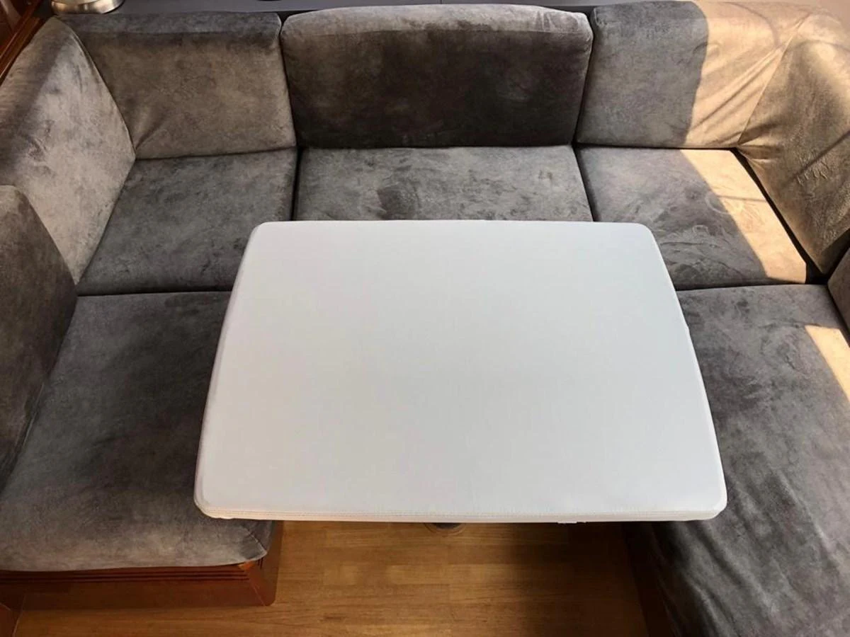 The image showcases a cozy saloon seating area with plush grey cushions and a central table. aboard RAINBOW Yacht for Sale
