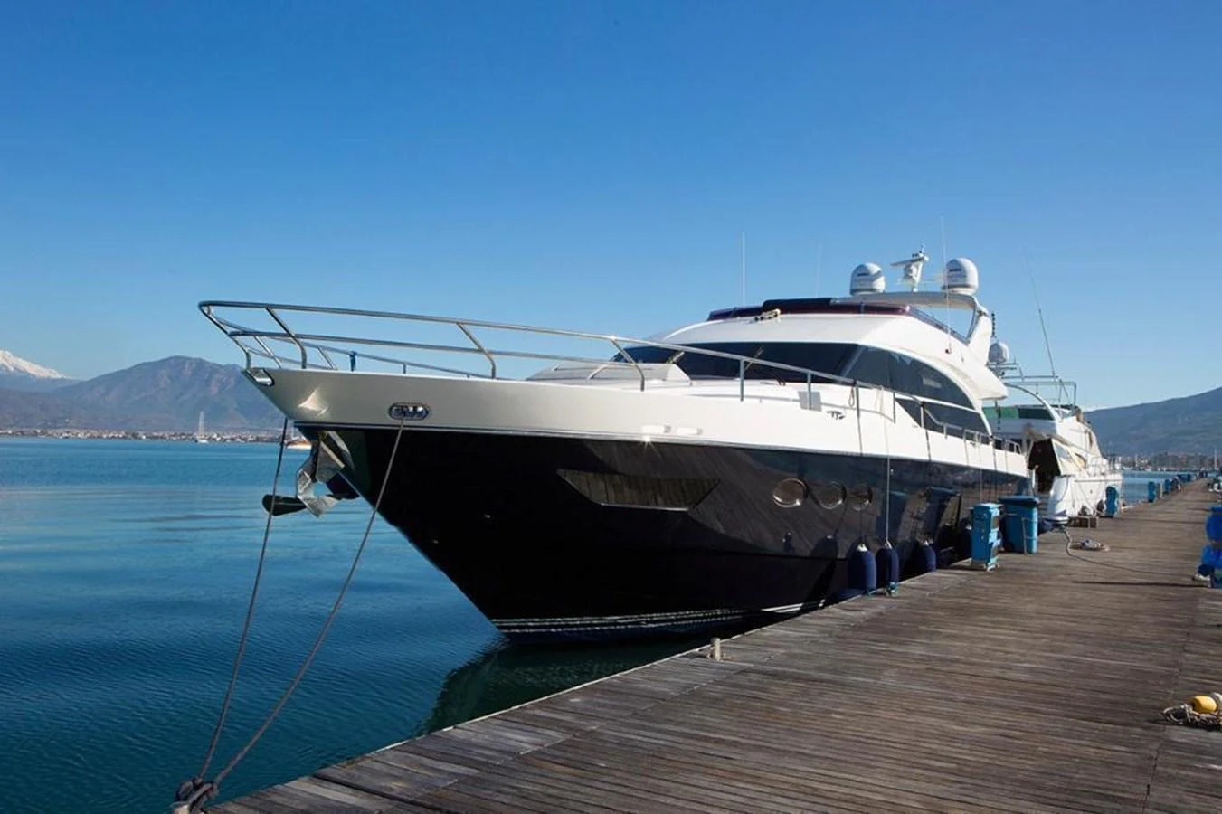 A sleek and modern yacht docked at a serene marina under a clear blue sky. aboard RAINBOW Yacht for Sale