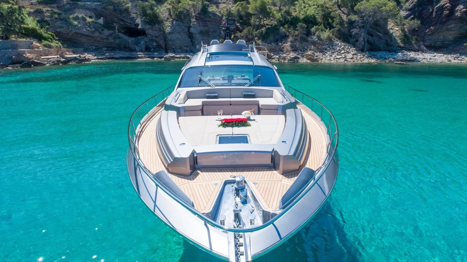 A sleek yacht is anchored in crystal-clear turquoise waters near a rocky shoreline. aboard DESERT STAR Yacht for Sale