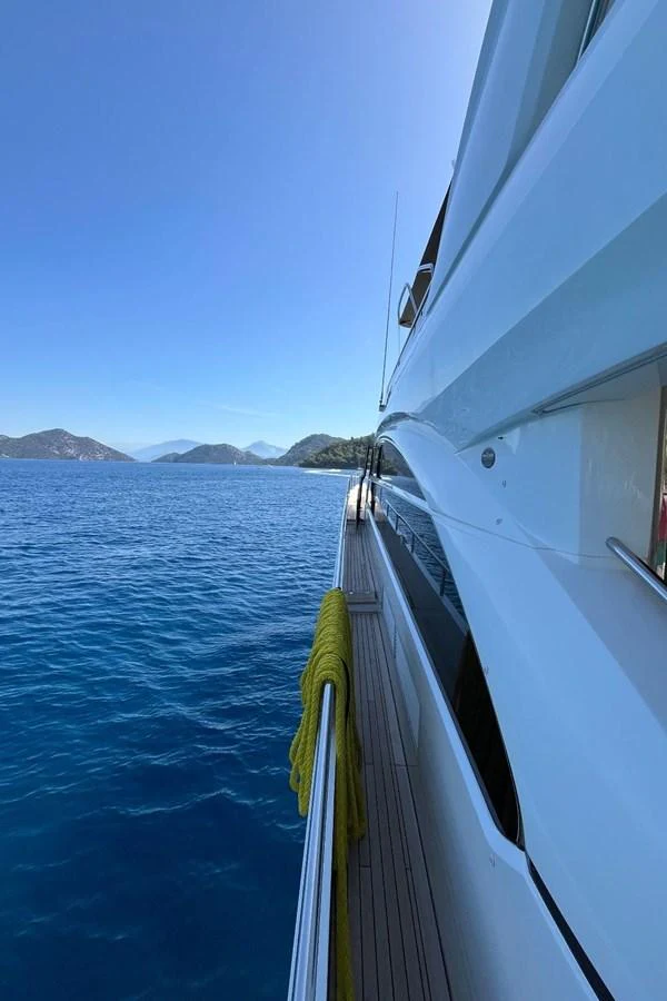 A sleek yacht cruising along a serene coastline with clear blue waters and distant mountains. aboard MS FELICE Yacht for Sale