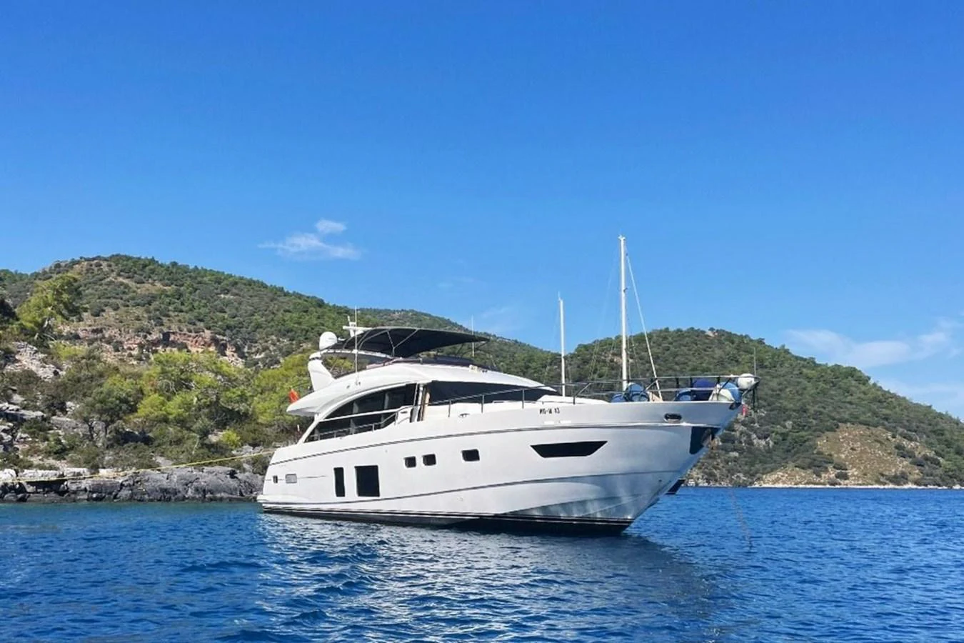 A sleek yacht is anchored in a serene bay with lush hills in the background. aboard MS FELICE Yacht for Sale