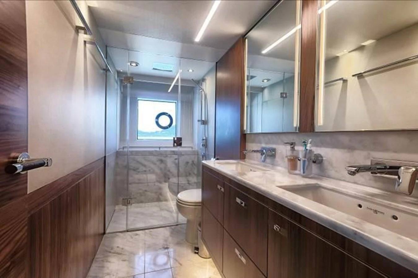 The yacht's bathroom features elegant wood paneling, a spacious marble countertop, and a glass-enclosed shower. aboard ANDAMAN PRINCESS Yacht for Sale
