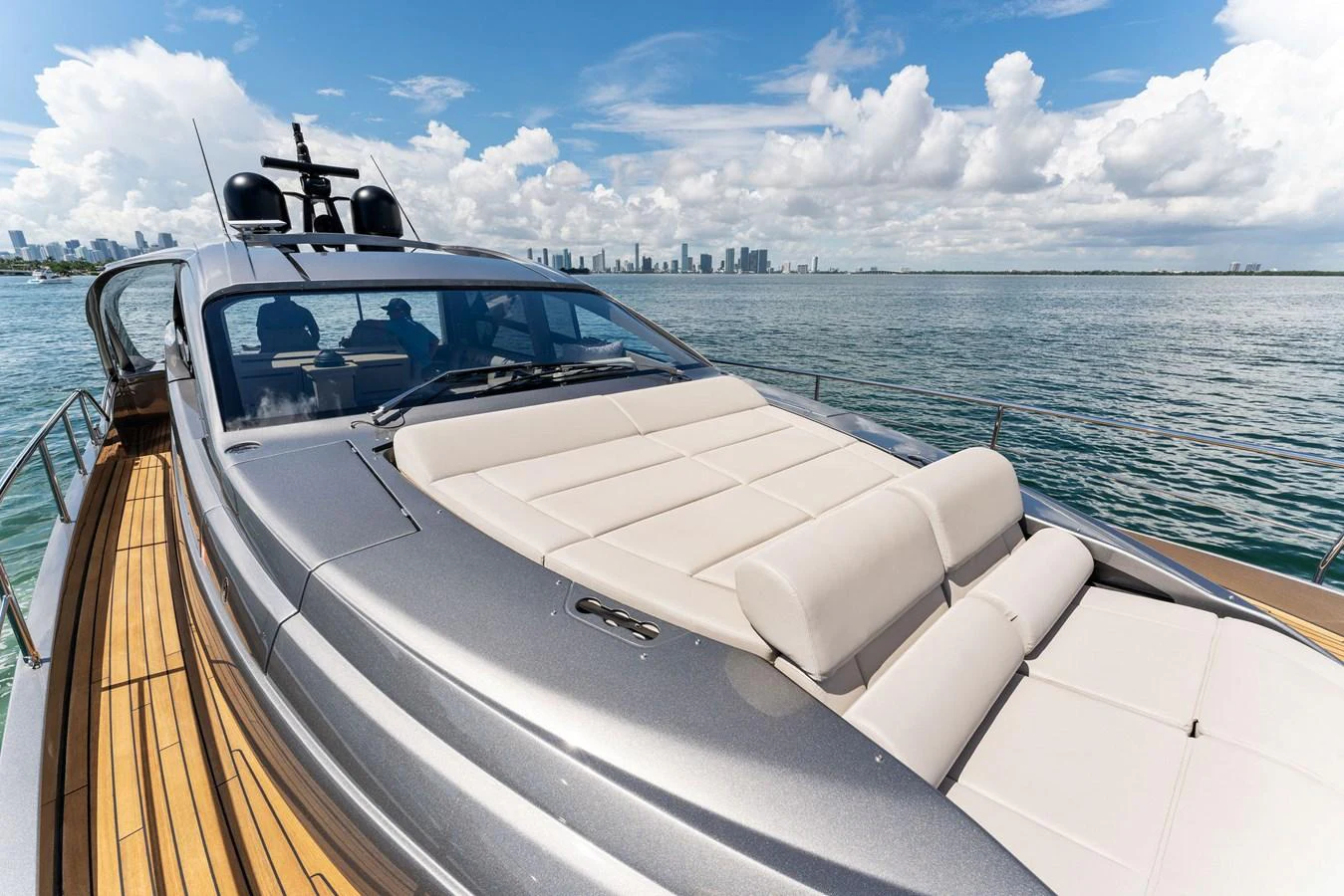 A sleek yacht with spacious sun loungers on the deck, cruising near a city skyline. aboard QUANTUM Yacht for Sale