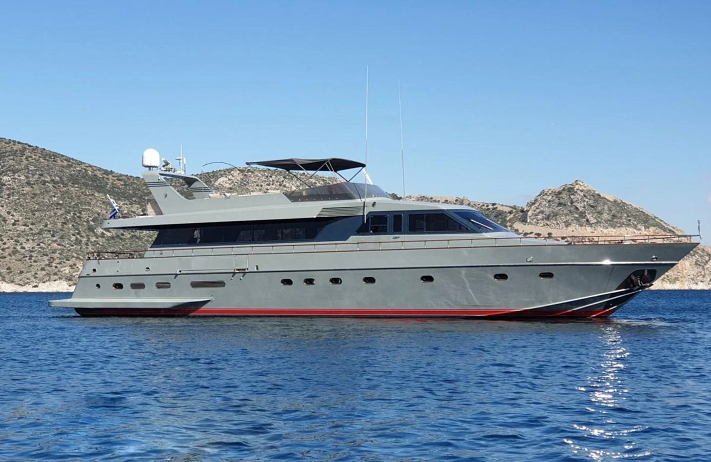 A sleek and modern yacht cruises on calm blue waters with a scenic rocky coastline in the background. aboard KISS Yacht for Sale