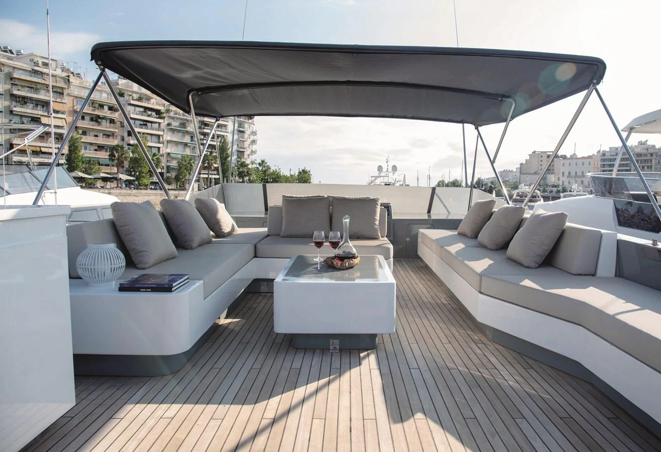 The flybridge offers a spacious and stylish lounging area with comfortable seating and a sleek coffee table under a shaded canopy. aboard KISS Yacht for Sale