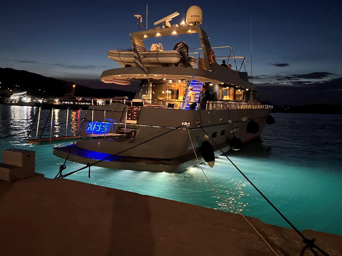 A luxurious yacht is docked at night, illuminated by elegant lighting that reflects on the water. aboard KISS Yacht for Sale