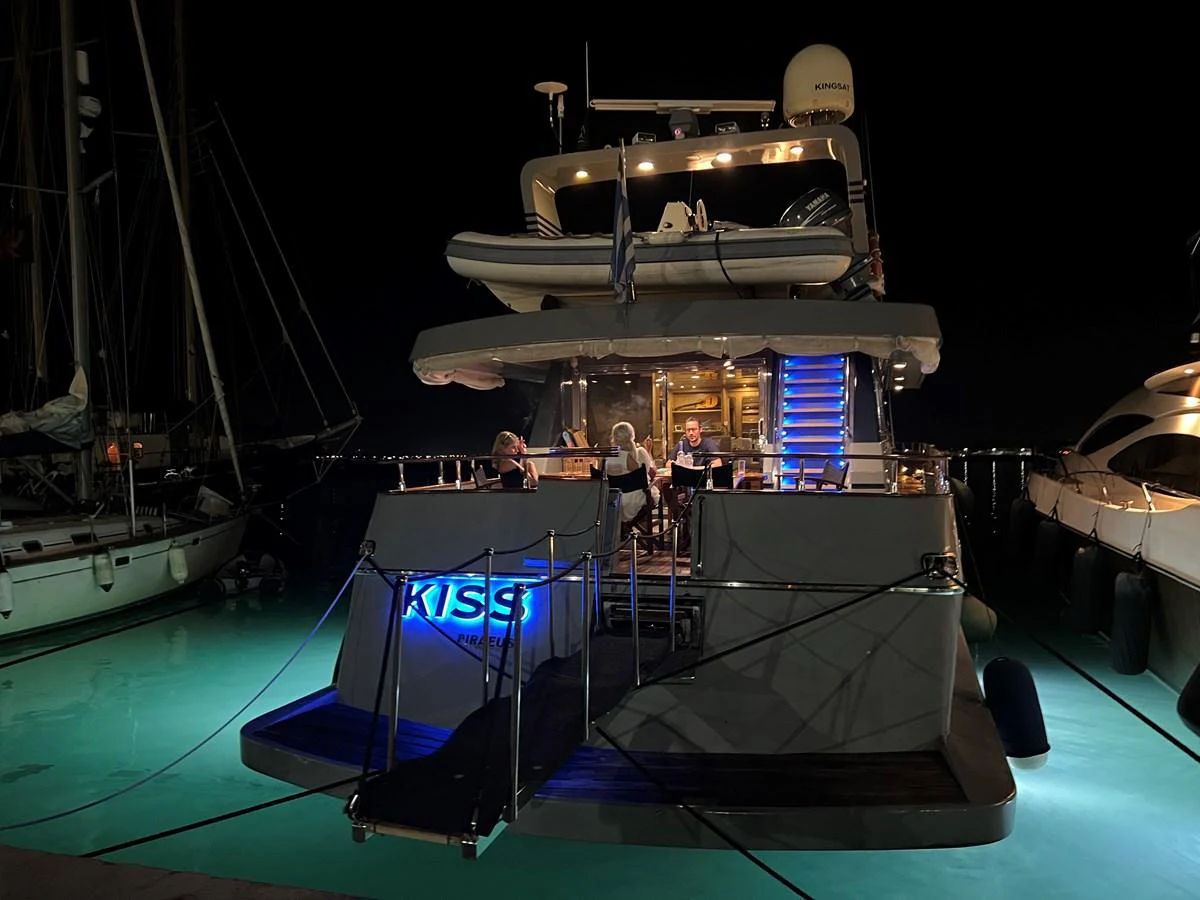 The yacht is docked at night, with a well-lit aft deck and a group of people enjoying the evening. aboard KISS Yacht for Sale
