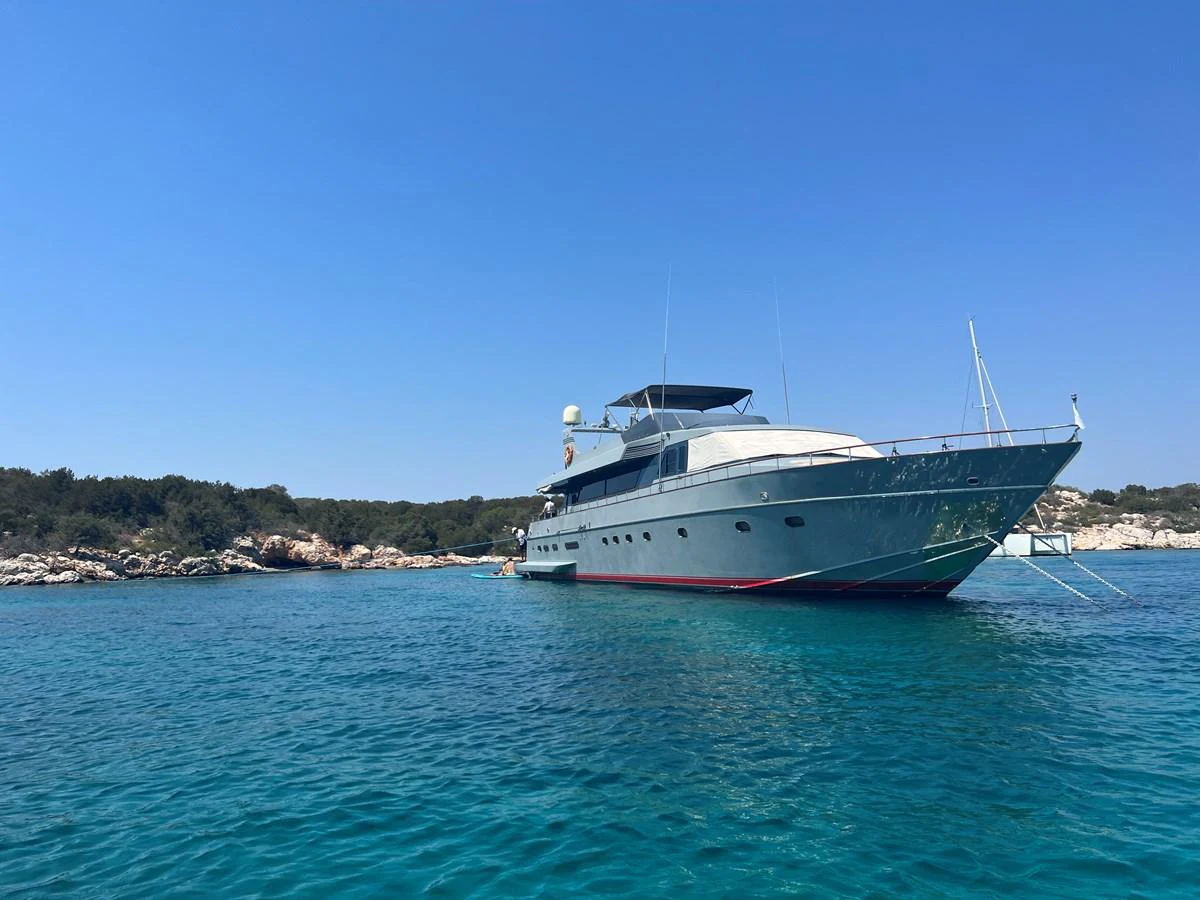 A sleek yacht is anchored in a serene, turquoise bay under a clear blue sky. aboard KISS Yacht for Sale