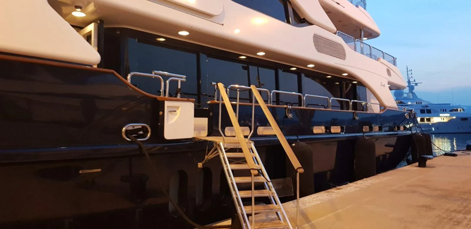 The yacht is docked at a marina, showcasing its sleek exterior design and elegant lighting. aboard MY SISA Yacht for Sale