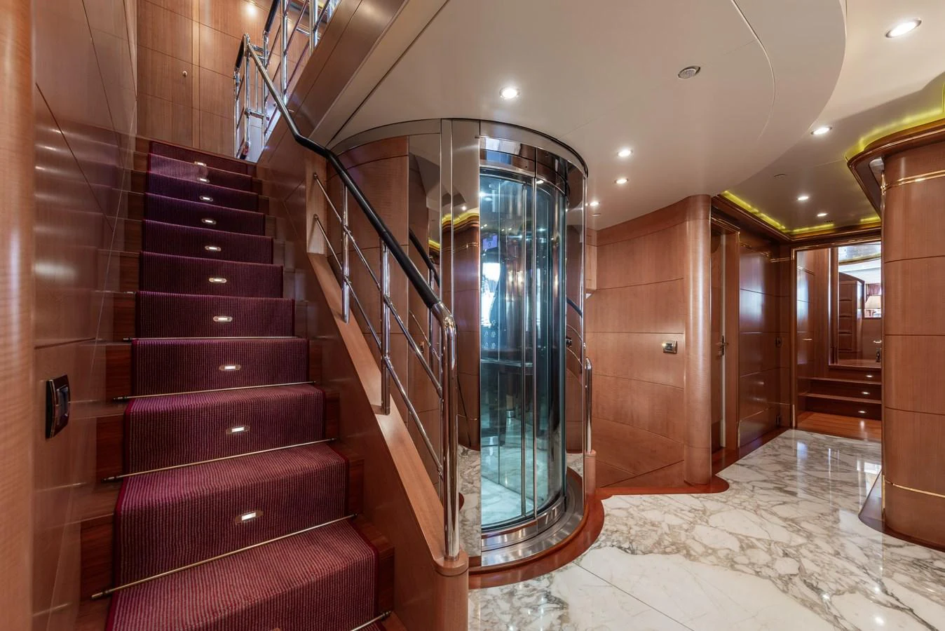 The yacht's interior features a luxurious staircase with a glass elevator and elegant wood paneling. aboard MY SISA Yacht for Sale