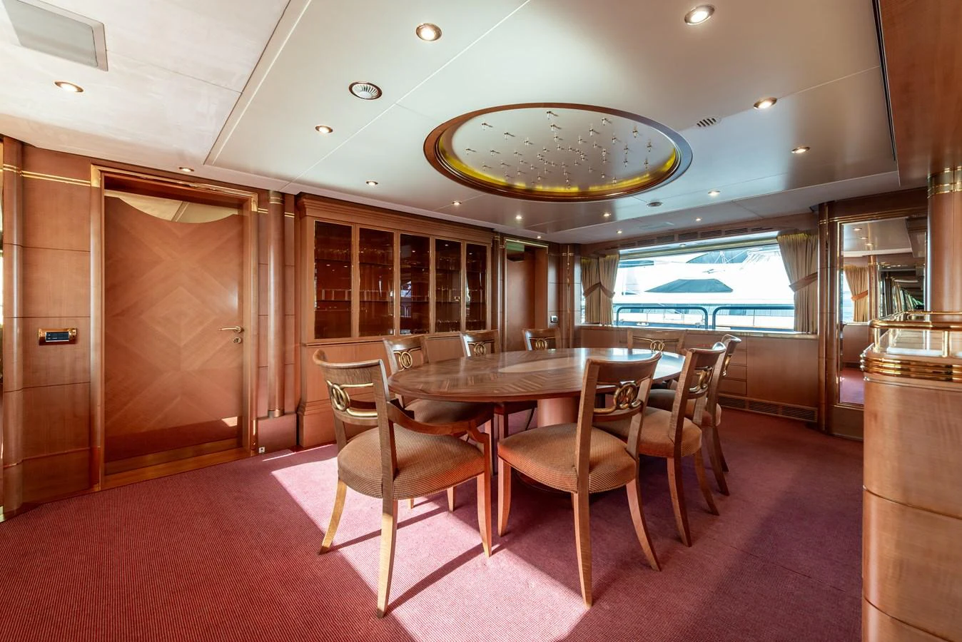 The yacht's dining area features elegant wooden furnishings and a large window with a view of the water. aboard MY SISA Yacht for Sale