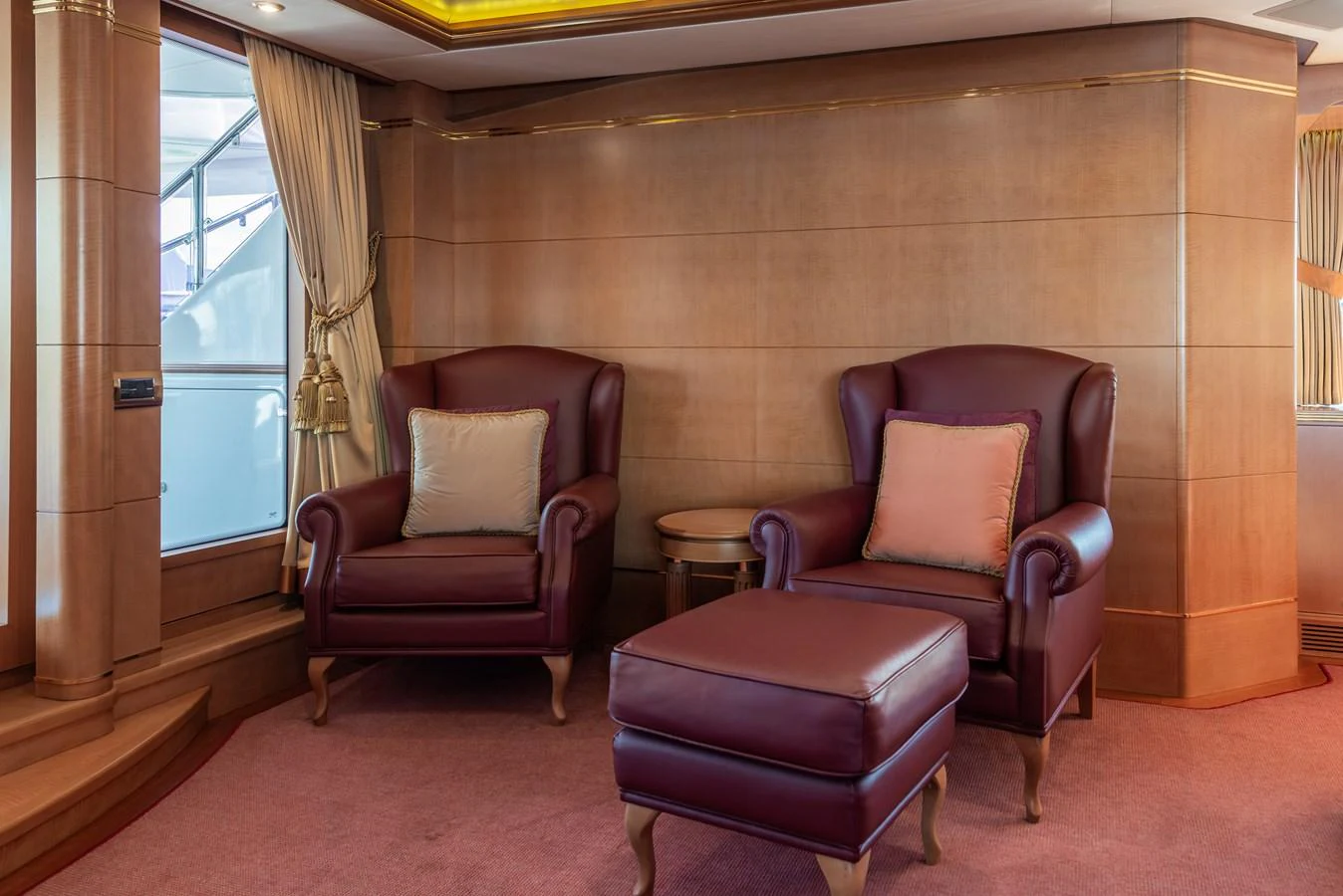 The image showcases a cozy seating area with two luxurious armchairs and an ottoman in a yacht's interior. aboard MY SISA Yacht for Sale