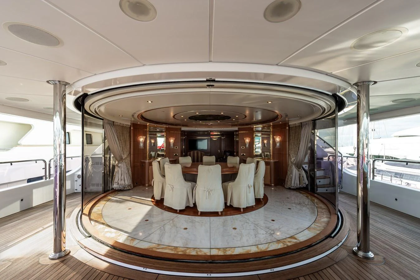 The yacht features an elegant dining area with a circular table and plush seating, surrounded by luxurious wood paneling and large windows. aboard MY SISA Yacht for Sale