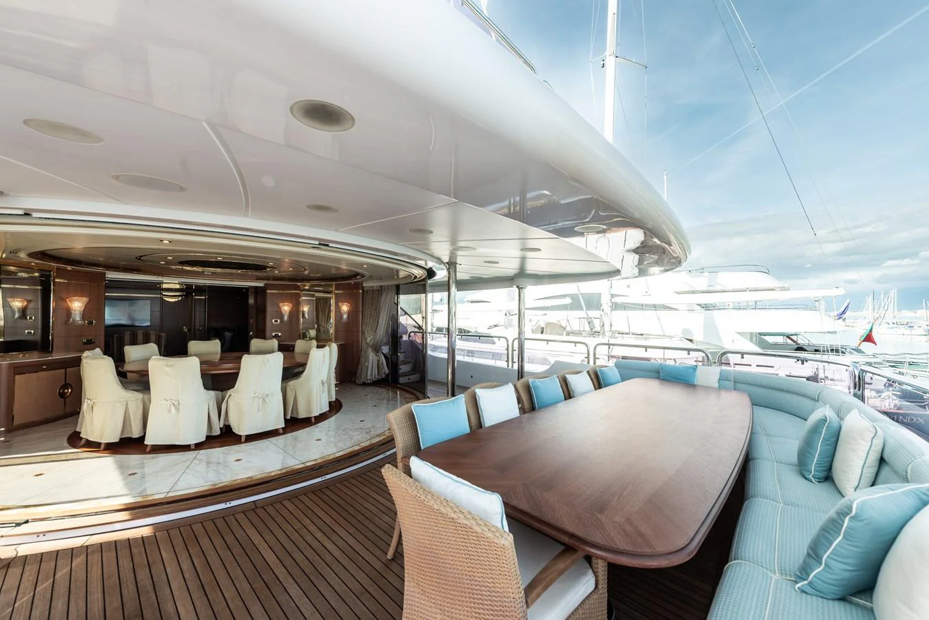 The aft deck features an elegant dining area with a large wooden table and comfortable seating, seamlessly blending indoor and outdoor spaces. aboard MY SISA Yacht for Sale