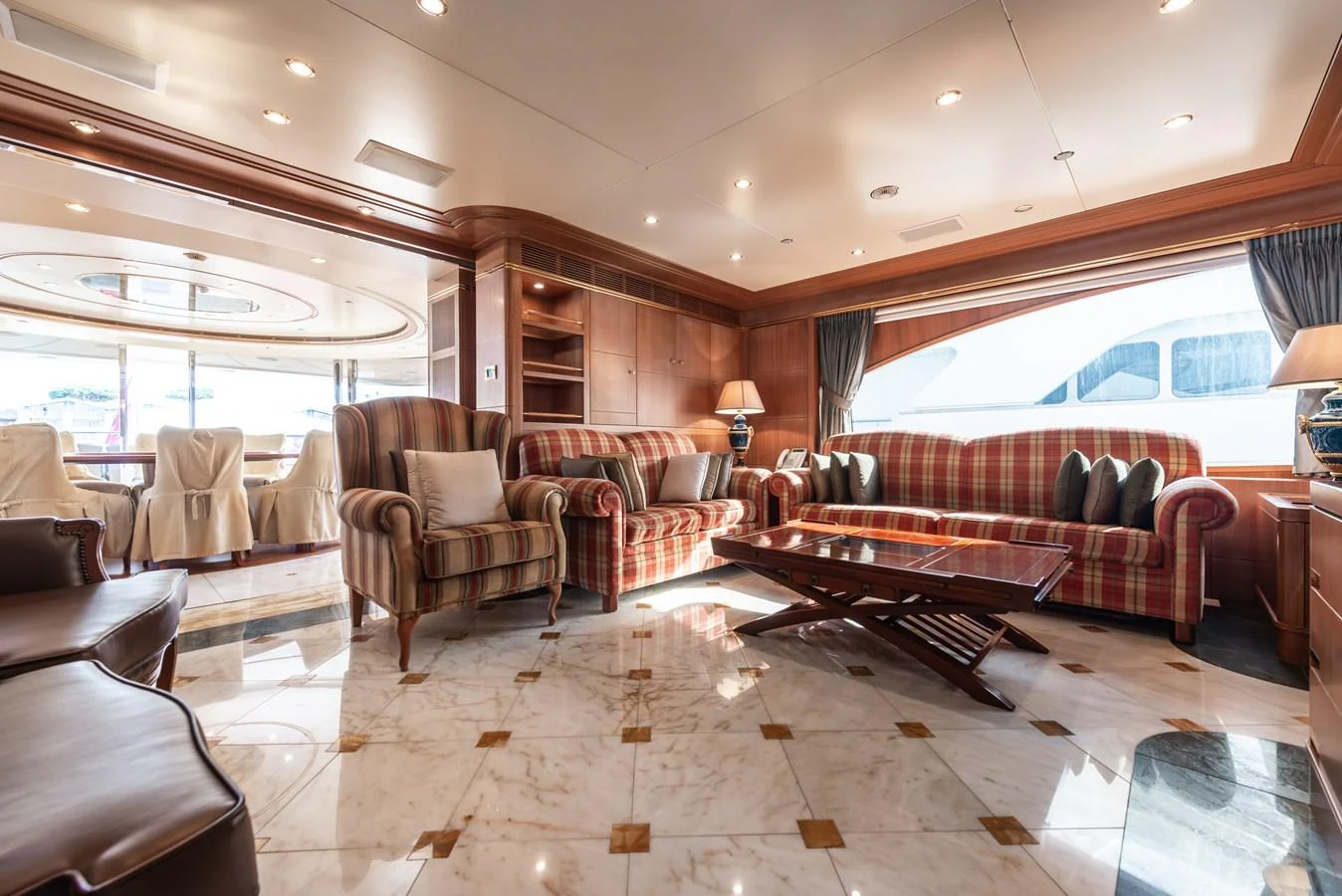 The yacht's salon features elegant seating with a mix of striped and plaid upholstery, complemented by a marble floor and ample natural light. aboard MY SISA Yacht for Sale