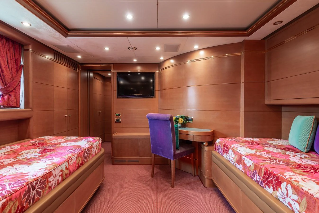 The guest stateroom features twin beds with vibrant floral bedding, a small desk, and a wall-mounted TV. aboard MY SISA Yacht for Sale