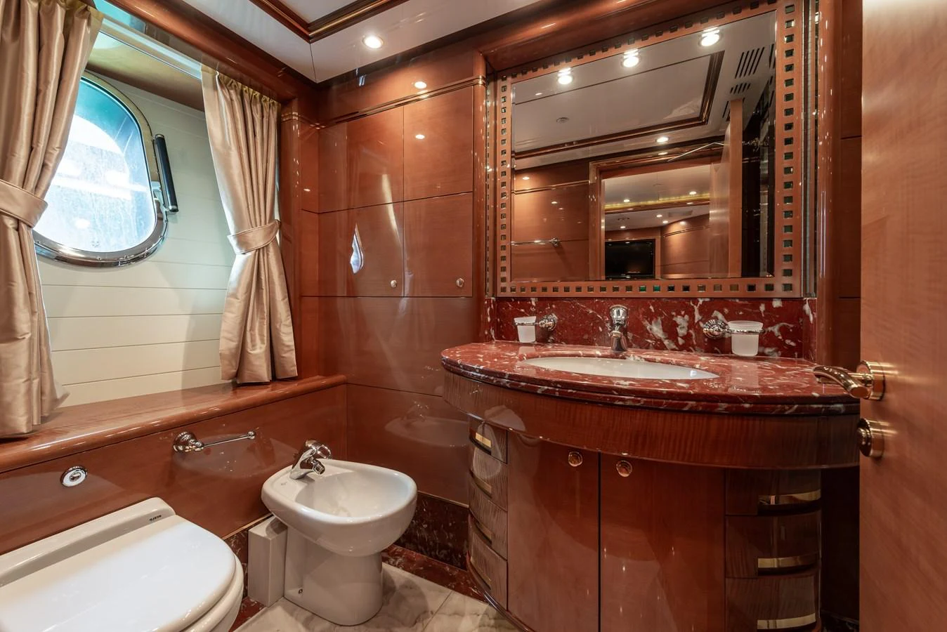 The yacht's bathroom features elegant wood paneling, a marble countertop, and a porthole window for natural light. aboard MY SISA Yacht for Sale