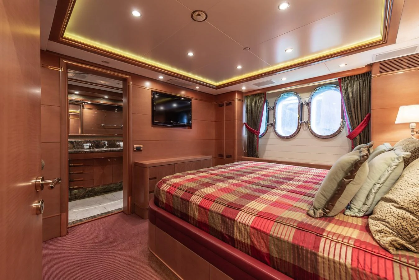 A luxurious stateroom featuring a large bed with plaid bedding, ambient lighting, and a view into the ensuite bathroom. aboard MY SISA Yacht for Sale