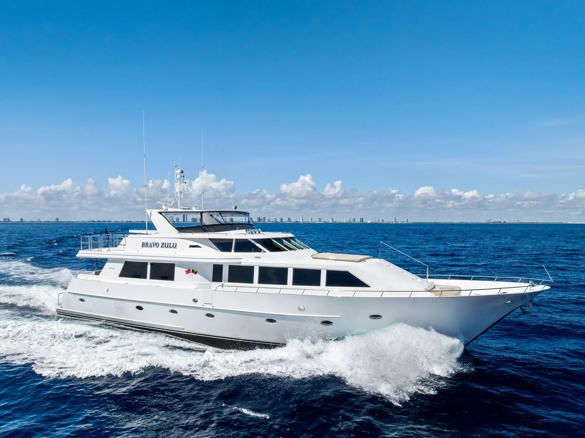 A sleek white yacht cruises swiftly through the open sea under a clear blue sky. aboard BRAVO ZULU Yacht for Sale