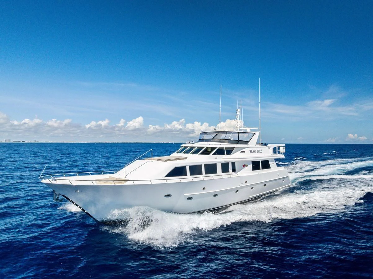 A sleek yacht cruises through the open water under a clear blue sky. aboard BRAVO ZULU Yacht for Sale