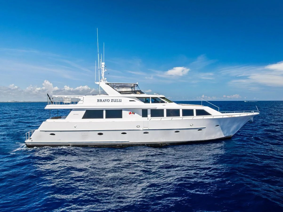 A sleek white yacht cruises on the open sea under a clear blue sky. aboard BRAVO ZULU Yacht for Sale