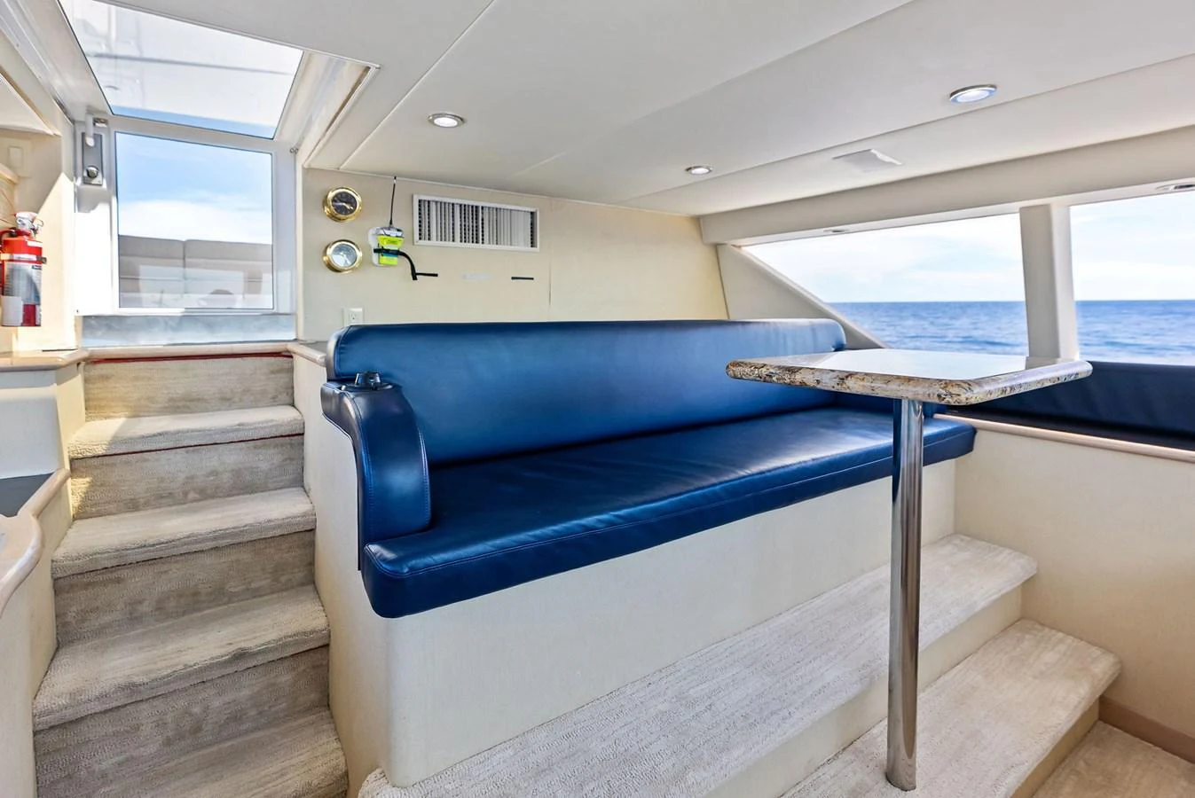 The yacht's salon features a comfortable blue leather seating area with a table, adjacent to a staircase leading to the upper deck. aboard BRAVO ZULU Yacht for Sale