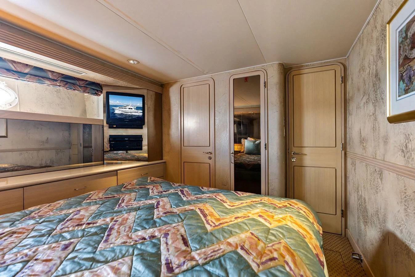 The stateroom features a cozy bed with a patterned quilt, a TV, and ample storage space. aboard BRAVO ZULU Yacht for Sale