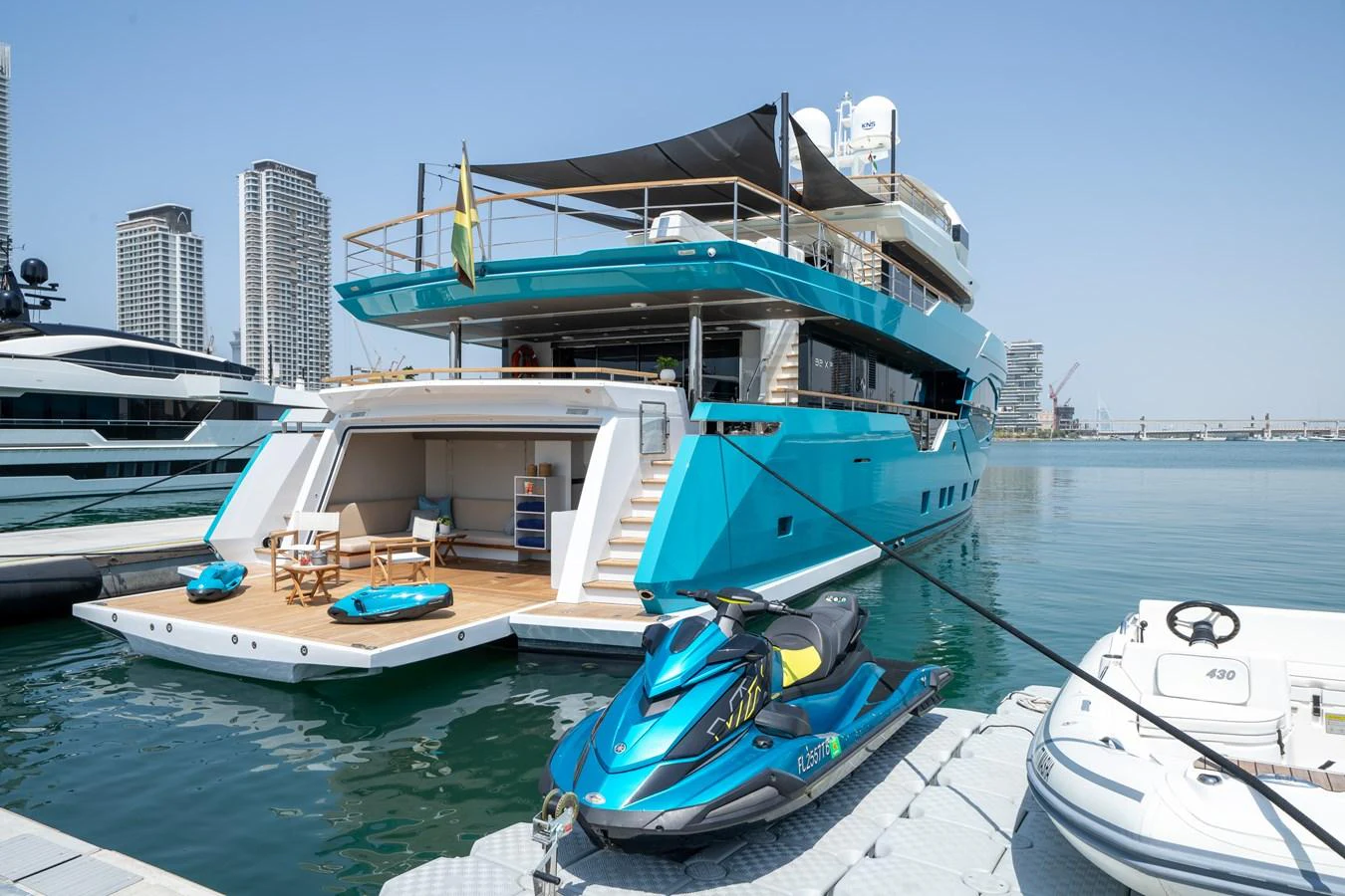The yacht is docked at a marina, showcasing its spacious aft deck and vibrant turquoise hull. aboard M/Y MASHA Yacht for Sale
