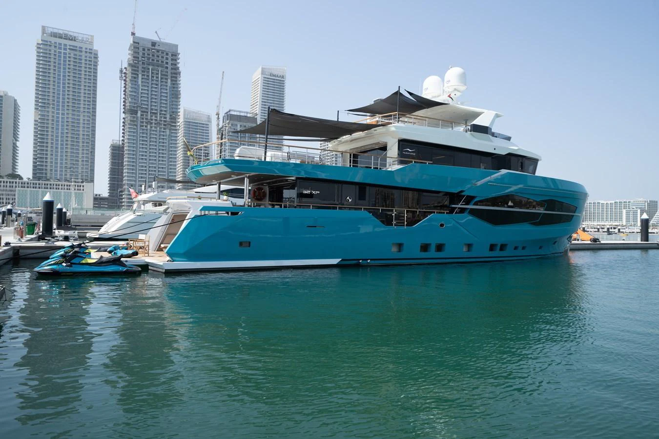 A sleek and modern yacht docked in a vibrant marina with a cityscape backdrop. aboard M/Y MASHA Yacht for Sale