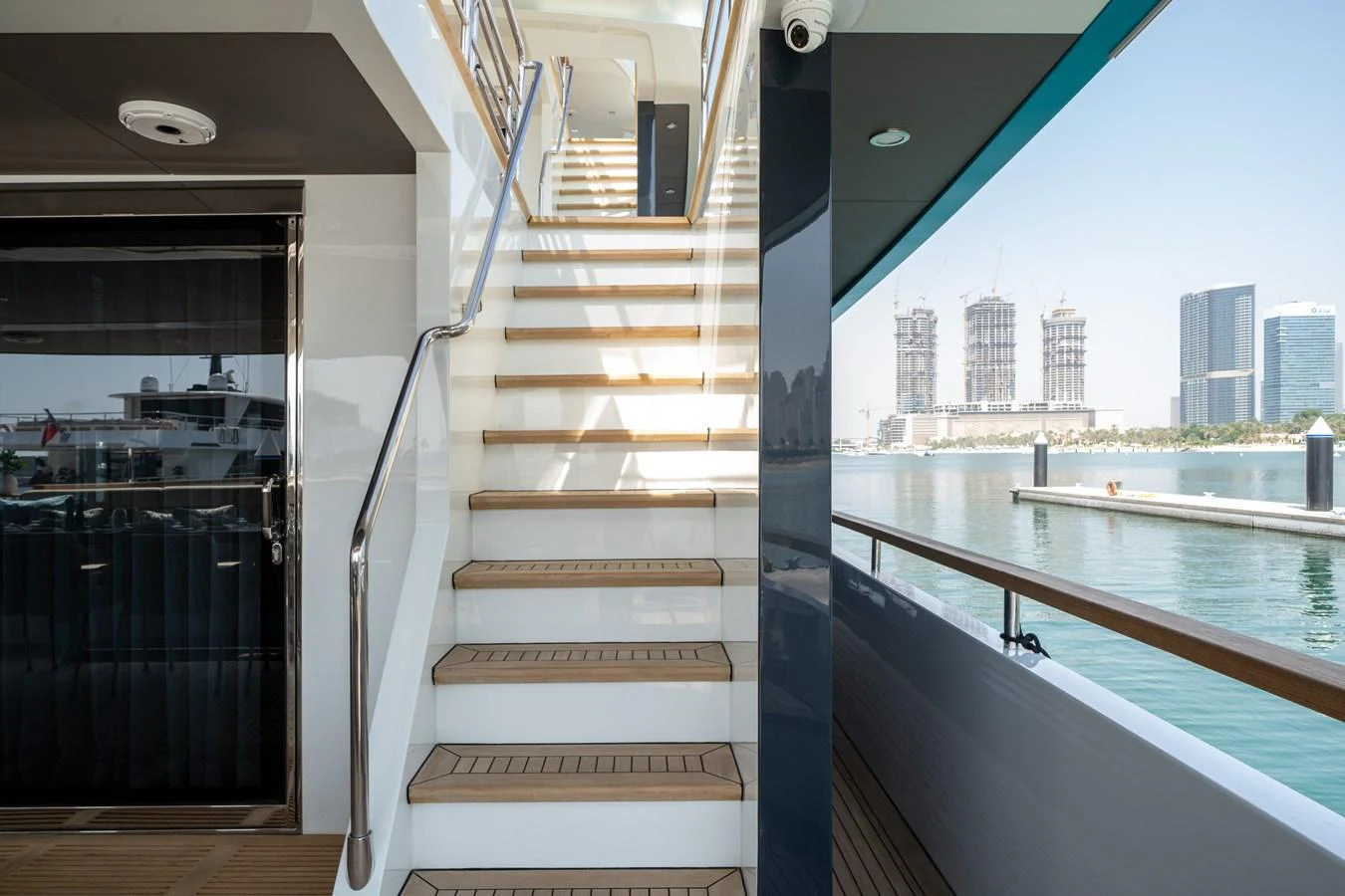A sleek side deck with a staircase leading to the upper level, offering a view of the water and cityscape. aboard M/Y MASHA Yacht for Sale
