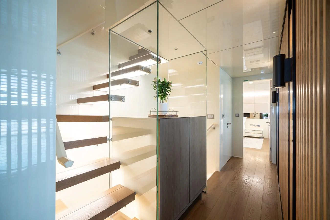 A modern and sleek interior staircase with glass railings and wooden steps, leading to a bright and airy space. aboard M/Y MASHA Yacht for Sale