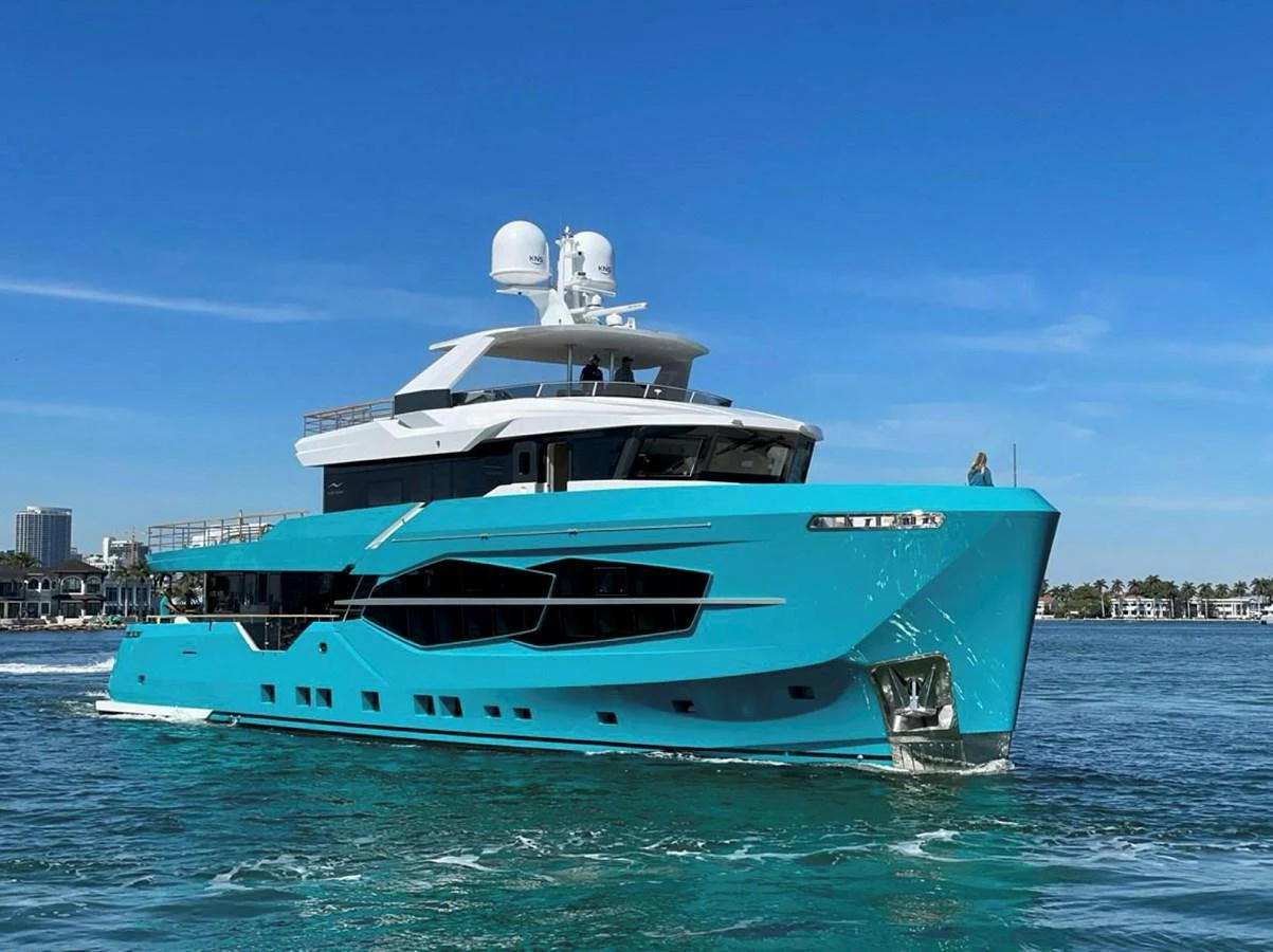 A sleek, modern yacht with a striking turquoise hull cruising on calm waters. aboard M/Y MASHA Yacht for Sale