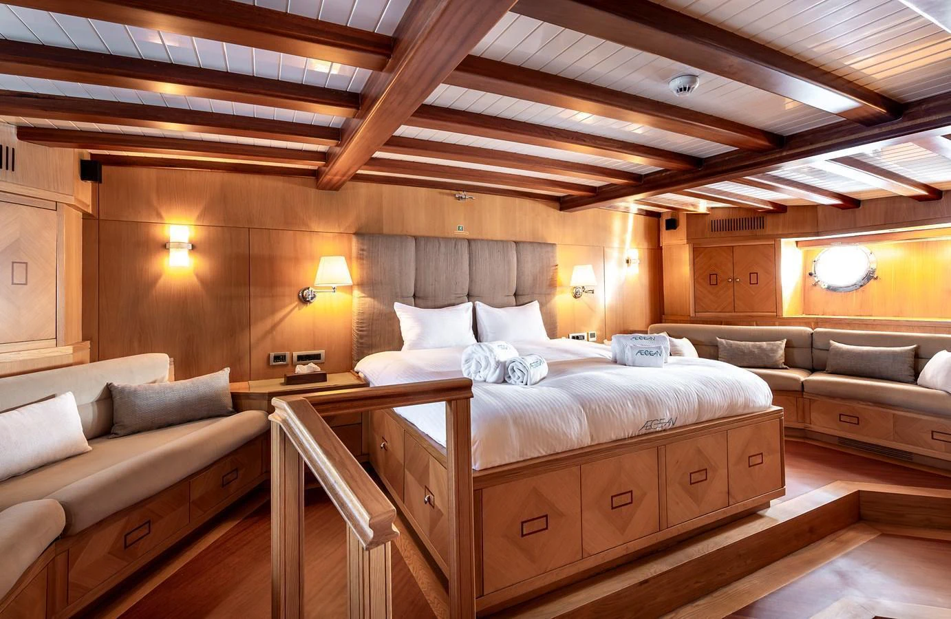 The master stateroom features a luxurious bed, warm wood finishes, and ample seating for relaxation. aboard AEGEAN Yacht for Sale