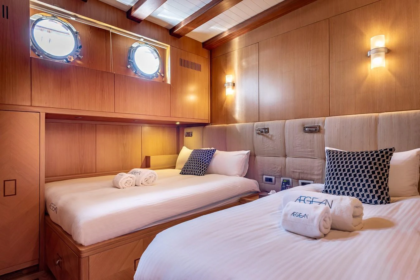 The guest stateroom features twin beds, warm wood paneling, and soft lighting for a cozy retreat. aboard AEGEAN Yacht for Sale