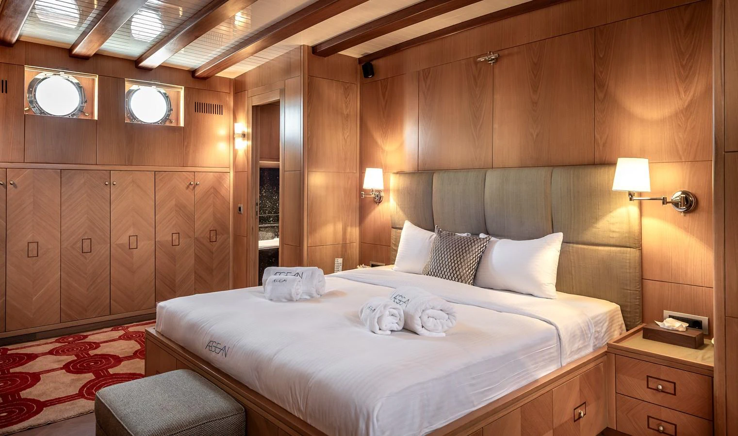 The master stateroom features a luxurious bed, warm wood paneling, and elegant lighting. aboard AEGEAN Yacht for Sale