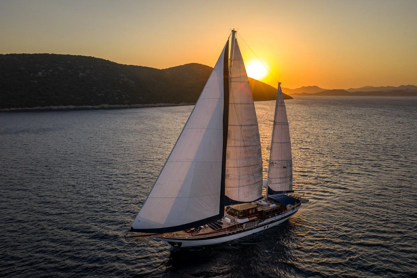 A stunning sailing yacht glides gracefully on the water at sunset. aboard AEGEAN Yacht for Sale
