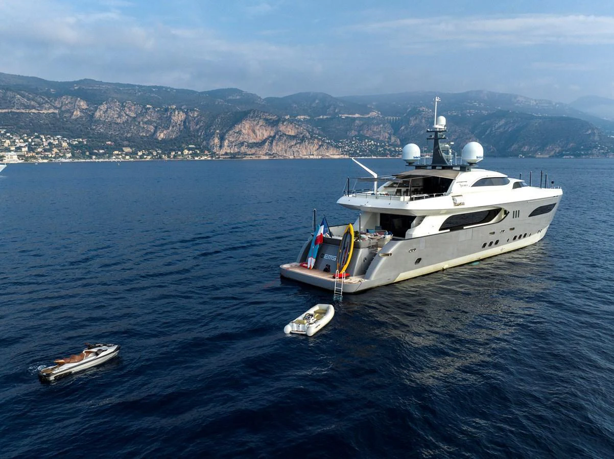 A luxurious yacht is anchored in a serene coastal area with tenders floating nearby. aboard GEMS II Yacht for Sale