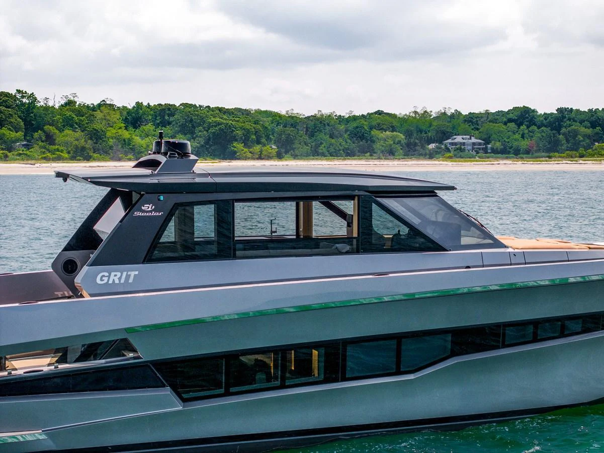A sleek, modern yacht cruising on calm waters with a lush, green shoreline in the background. aboard GRIT Yacht for Sale