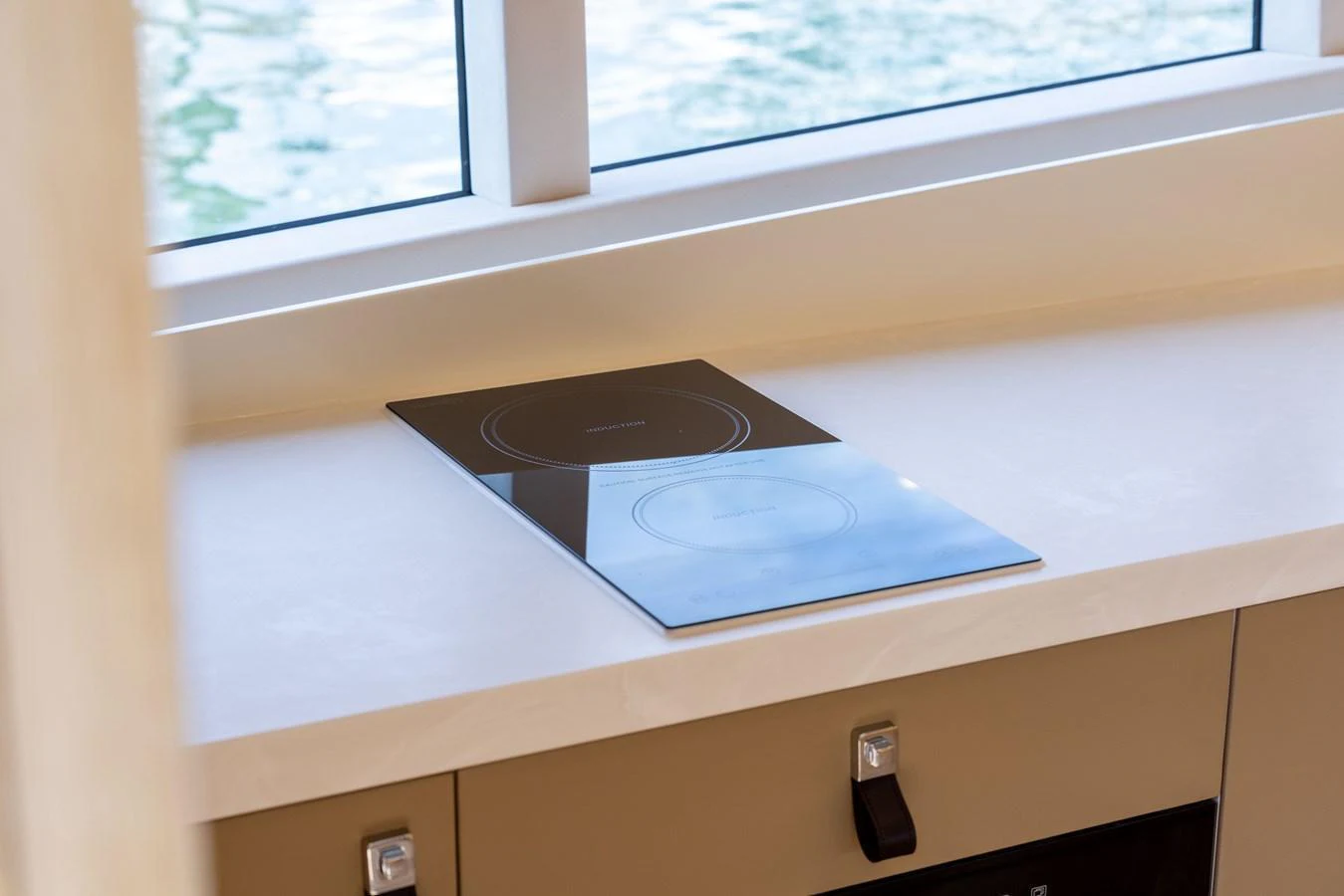 The image showcases a sleek and modern galley with a built-in cooktop and a view of the water through the window. aboard GRIT Yacht for Sale